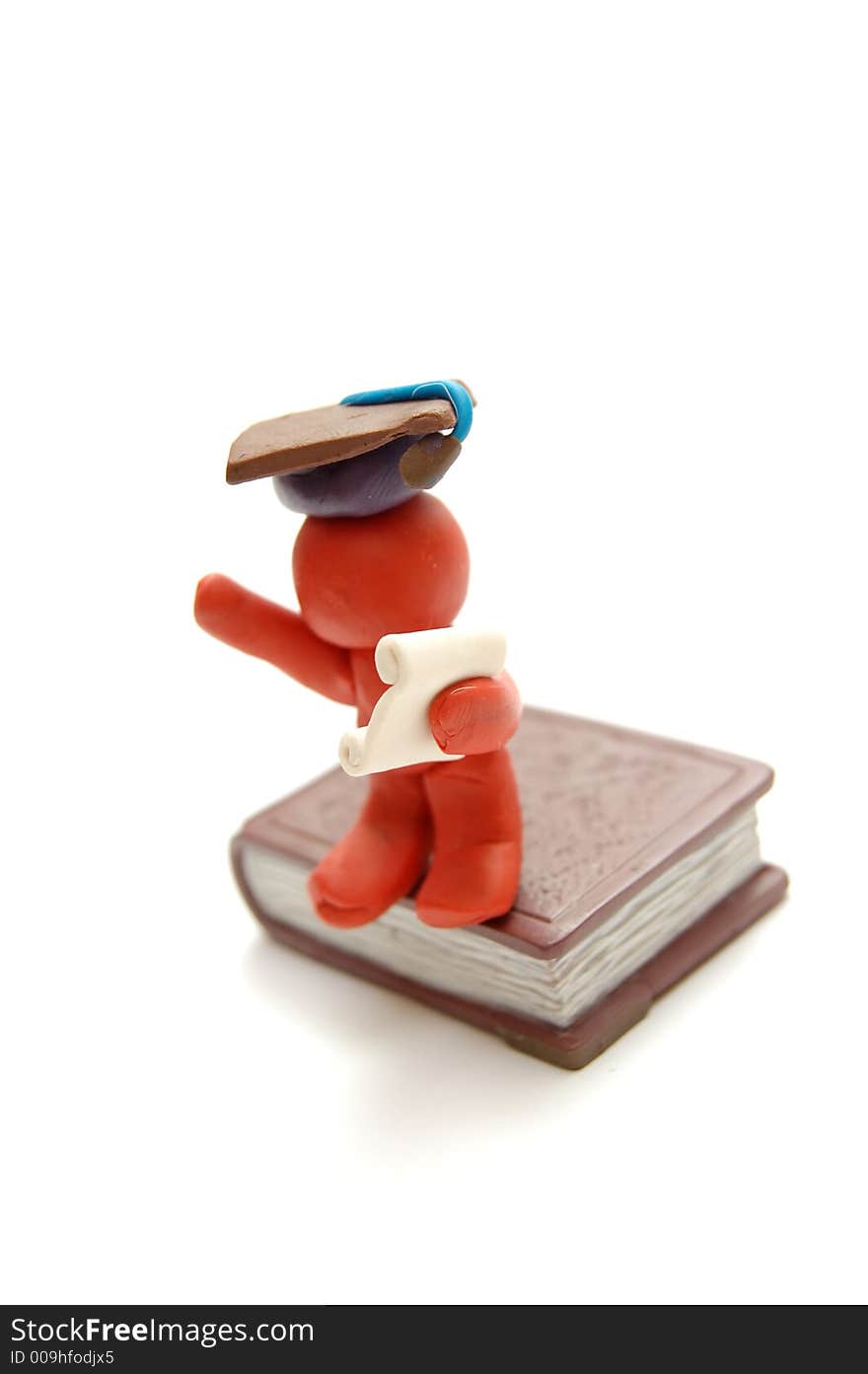 Plasticine figure celebrating graduation with certificate and student hat sitting on book. Plasticine figure celebrating graduation with certificate and student hat sitting on book