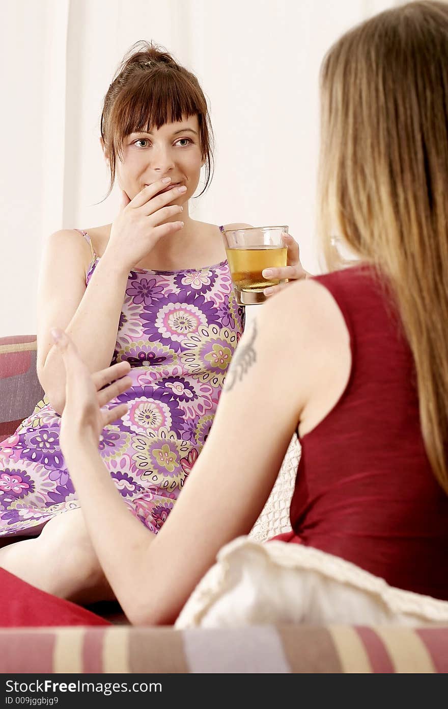 Two girls, young women chatting on a sofa and drinking