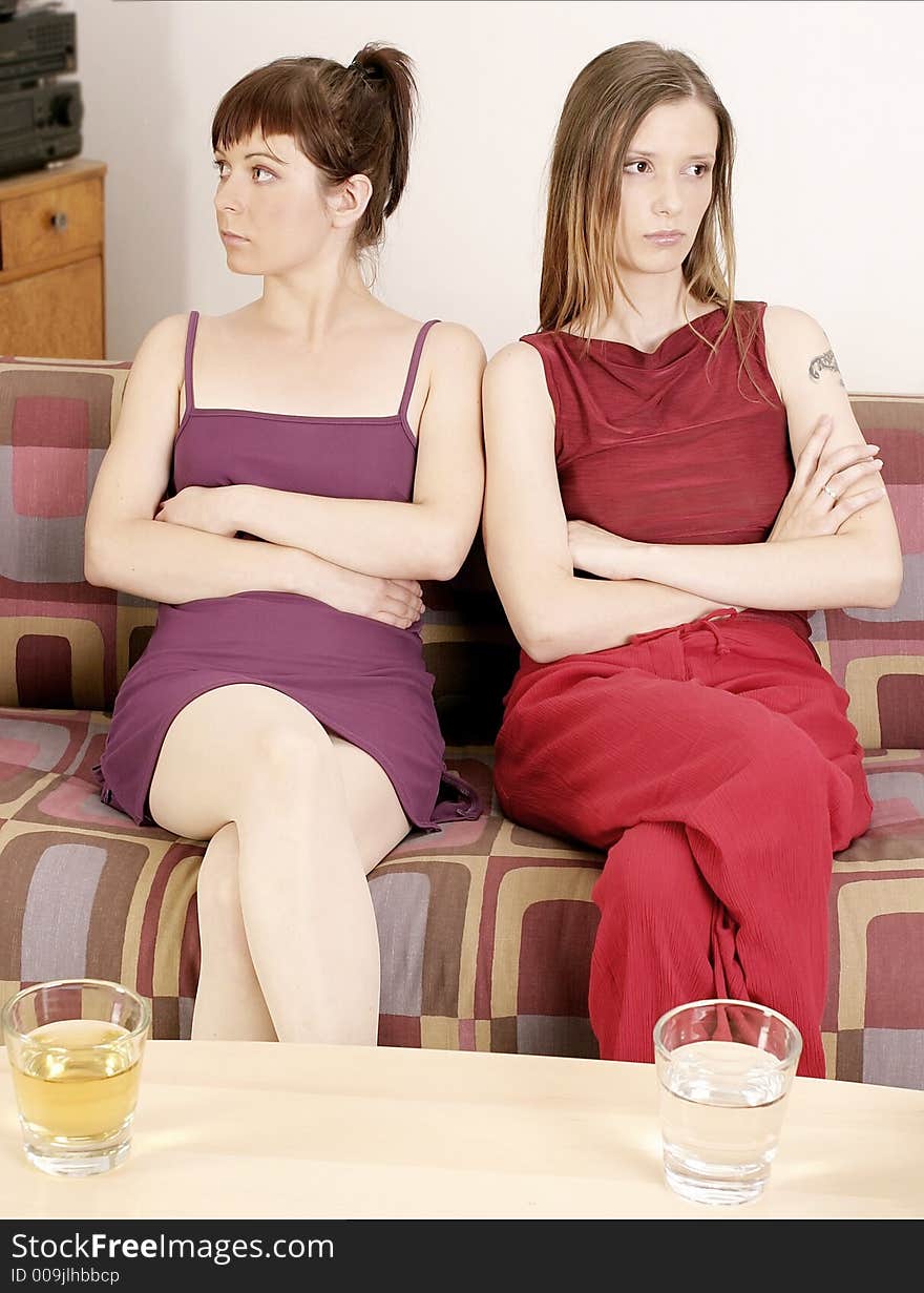 Two girls young women sitting on a sofa, looking opposite direction