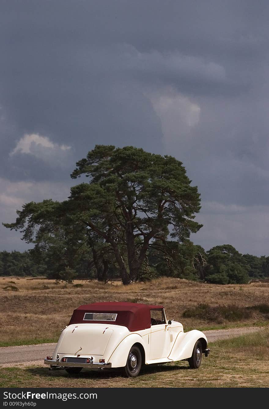 An old-timer car parked next to the road with a forest and sky background. An old-timer car parked next to the road with a forest and sky background