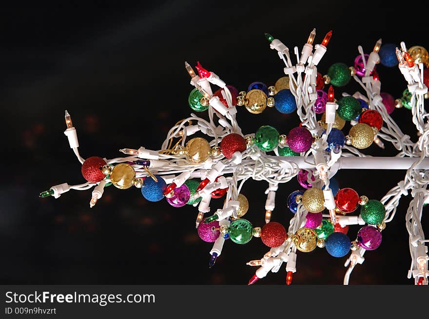 A white wire christmas tree with lights and multi colored garland against a black background