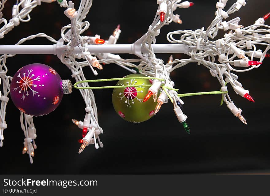 A white wire christmas tree with lights and purple and green ball ornamnets against a black background. A white wire christmas tree with lights and purple and green ball ornamnets against a black background