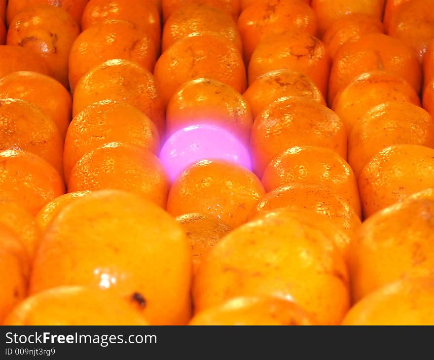 Purple glowing mandarin orange in rows of 'normal' mandarin oranges. Purple glowing mandarin orange in rows of 'normal' mandarin oranges.