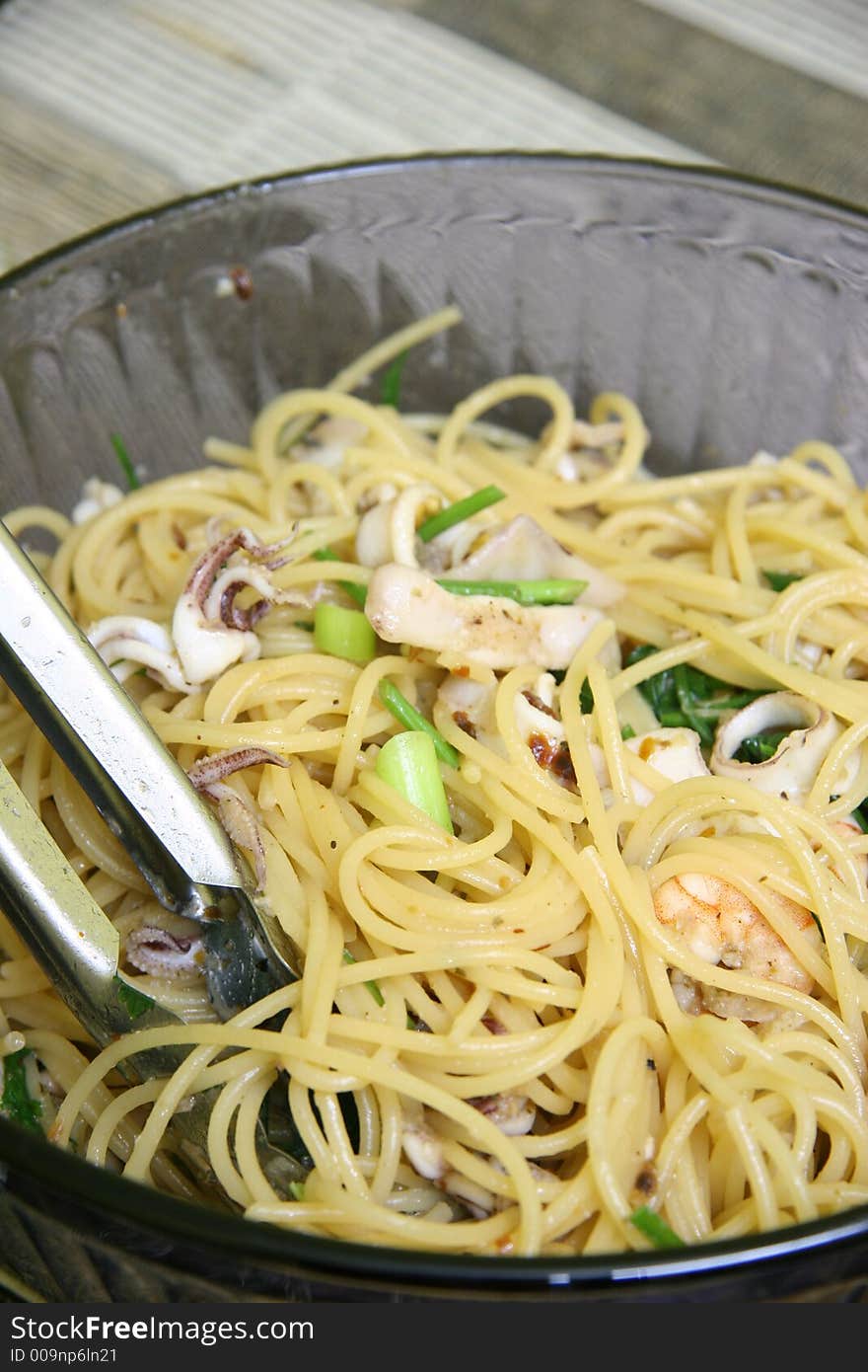 Seafood pasta with green leafy vegetables in a deep glass bowl