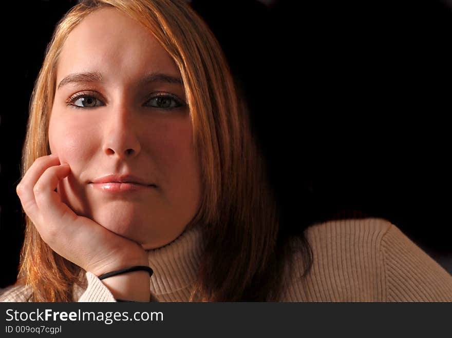 Attractive young woman with her chin resting on her hand against a black background