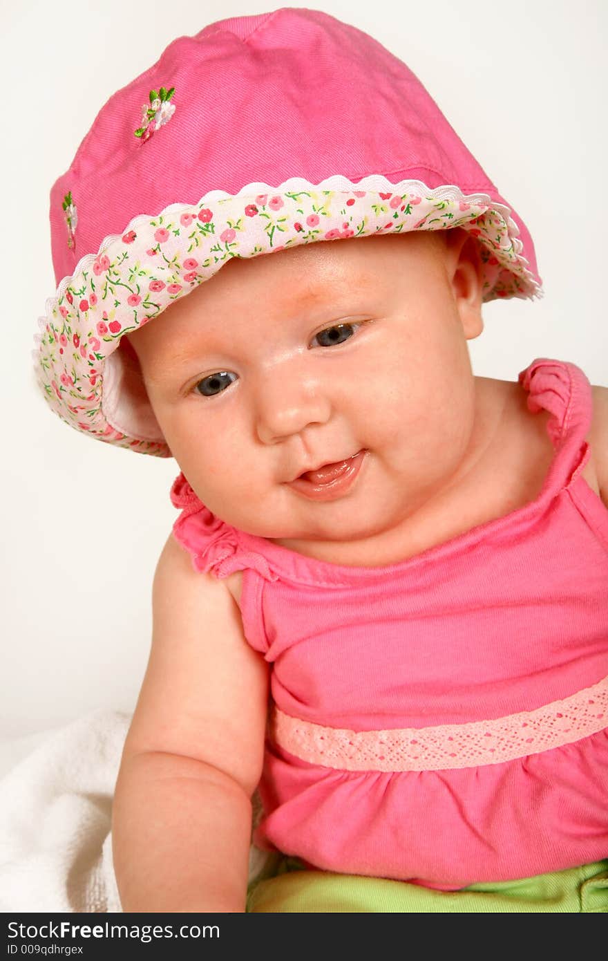 A baby girl sitting with a hat on her head. A baby girl sitting with a hat on her head