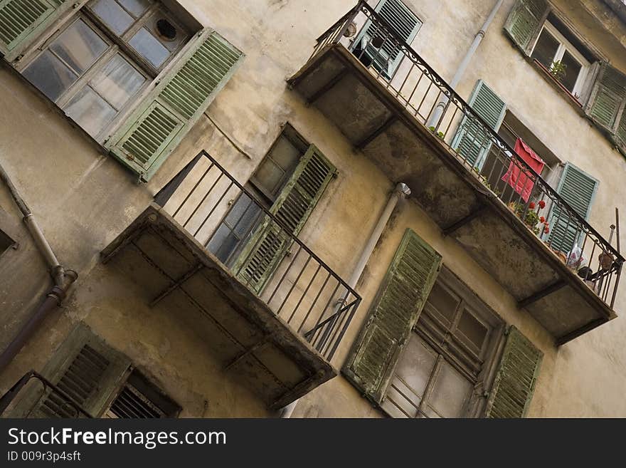 Looking up from the street at shuttered windows and balconies of a cream-coloured residential building in Old Nice, France. Washing is out to dry, plants are on display. Everything looks rather run down and in need of a clean or a fresh lick of paint. Looking up from the street at shuttered windows and balconies of a cream-coloured residential building in Old Nice, France. Washing is out to dry, plants are on display. Everything looks rather run down and in need of a clean or a fresh lick of paint.