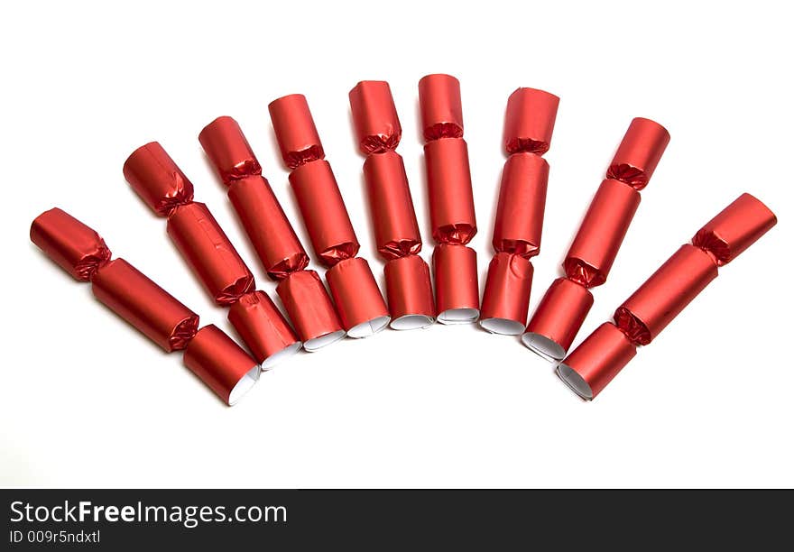 An arrangment of red Christmas English party crackers isolated over white. Party Crackers are an old English party favor idea and tradition. They are festively wrapped cardboard cylinders that can be filled with all manner of treasures and trinkets and tied off at the ends. A cracker snap is inserted which, when pulled from both ends, pops loudly.