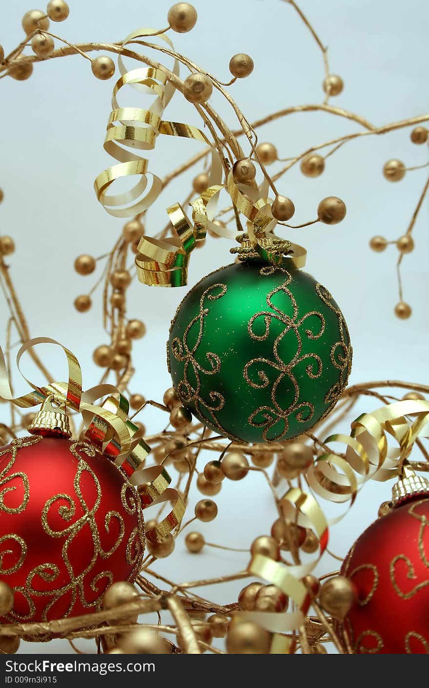 A trio of red and green Christmas ornaments decorated with ribbons and gold berries. A trio of red and green Christmas ornaments decorated with ribbons and gold berries