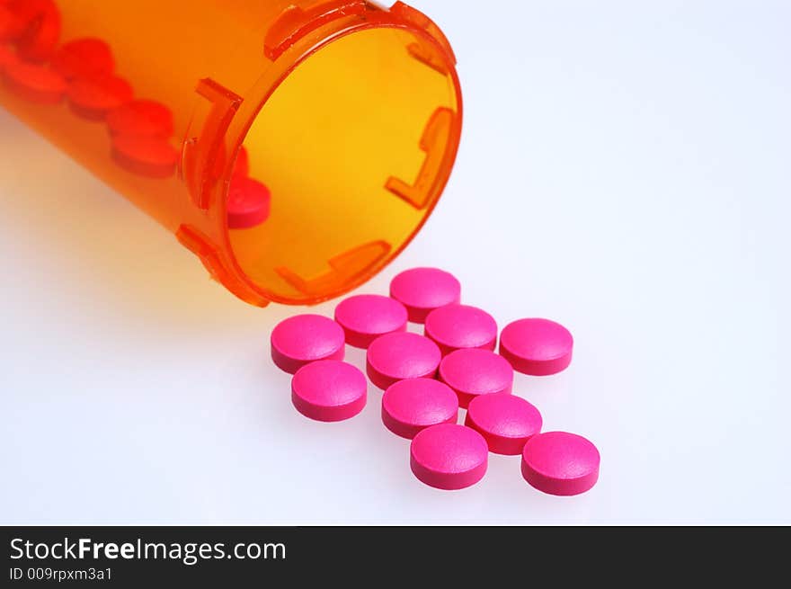 Magenta colored pills on white surface in front of the medicine bottle they spilled from. Magenta colored pills on white surface in front of the medicine bottle they spilled from