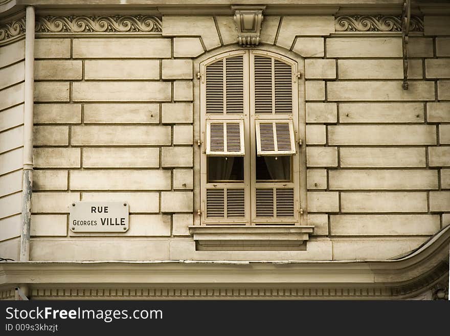 An old shuttered window of an off-white ornate building in Nice, France. The main shutters are closed over the window, but two of the smaller shutters are raised. A sign showing the name of the road Rue Georges Ville is visible. An old shuttered window of an off-white ornate building in Nice, France. The main shutters are closed over the window, but two of the smaller shutters are raised. A sign showing the name of the road Rue Georges Ville is visible.