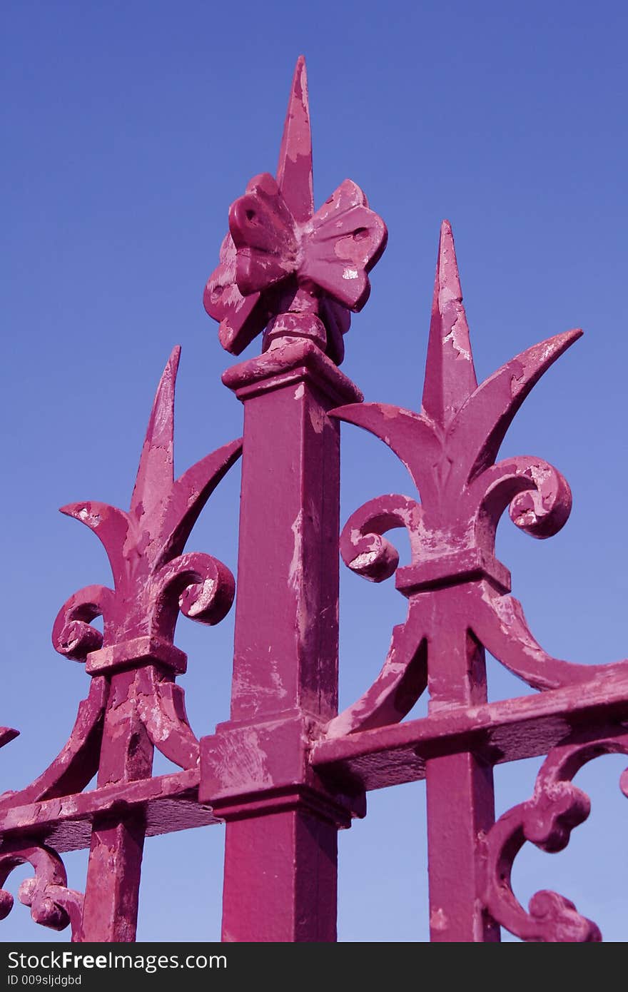 Red Metal Fence Top In Front Of Clear Blue Sky