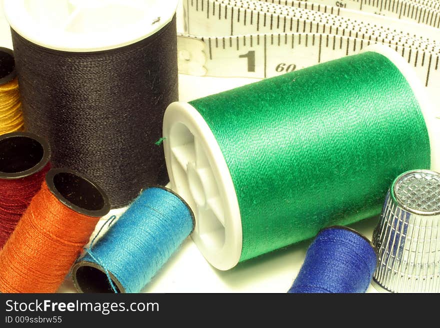 This is a close up image of spools of thread, a thimble, and tape measure. This is a close up image of spools of thread, a thimble, and tape measure.