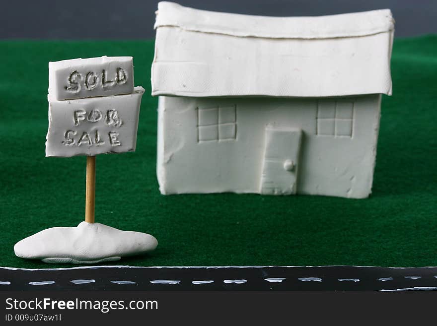 A whimsical clay house with a for sale sign and a sold sign. A whimsical clay house with a for sale sign and a sold sign