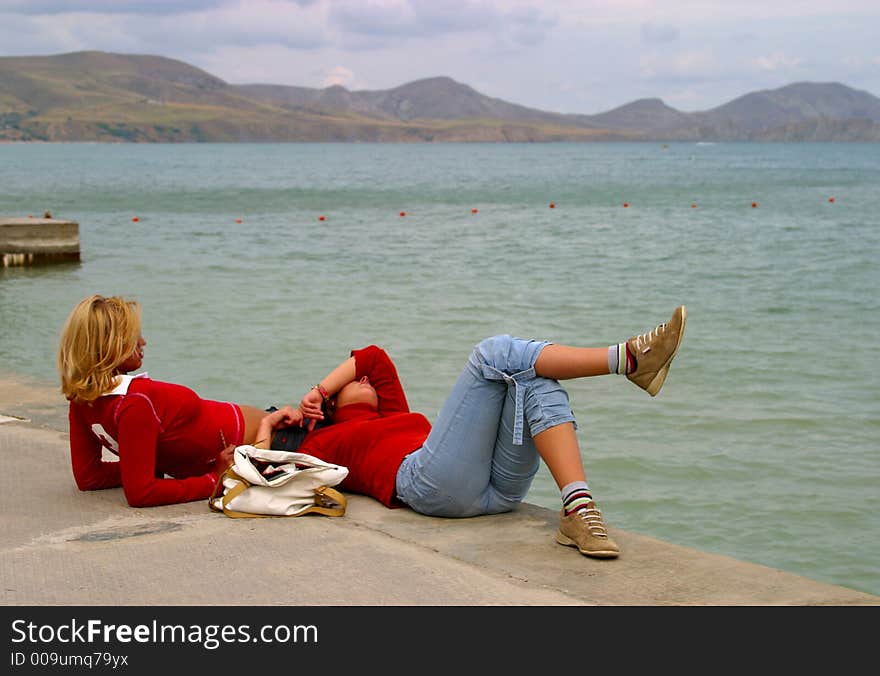 Girlfriends have a rest at edge of a pier. Girlfriends have a rest at edge of a pier