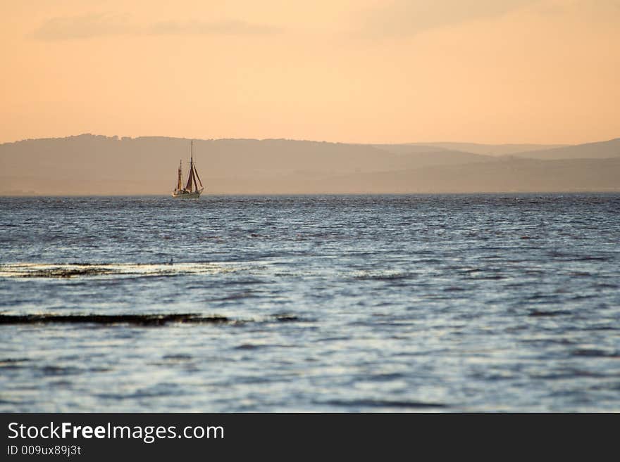 Sailing ship in the Bristol Channel as the sun goes down and bathes the scene in orange light. Sailing ship in the Bristol Channel as the sun goes down and bathes the scene in orange light