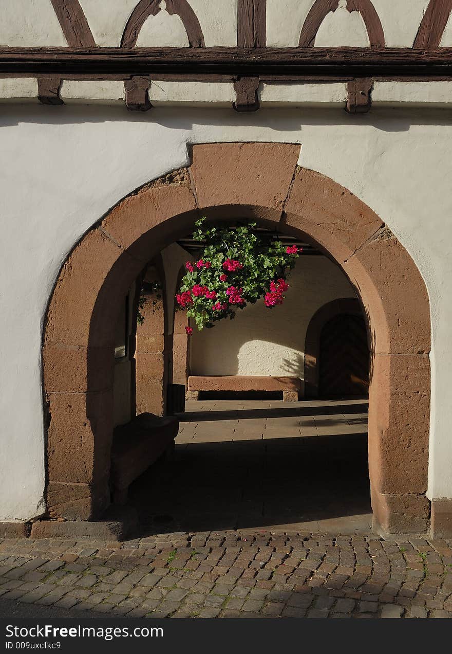 The outside of a town hall in a southern German town is made of a half-timbered structure and an old arch with a pot-flower hanging in its middle. The outside of a town hall in a southern German town is made of a half-timbered structure and an old arch with a pot-flower hanging in its middle.