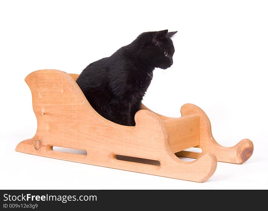 A black cat sits in a wooden sled on a white background. A black cat sits in a wooden sled on a white background