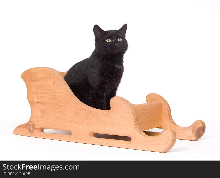 A black cat sits in a wooden sled on a white background. A black cat sits in a wooden sled on a white background