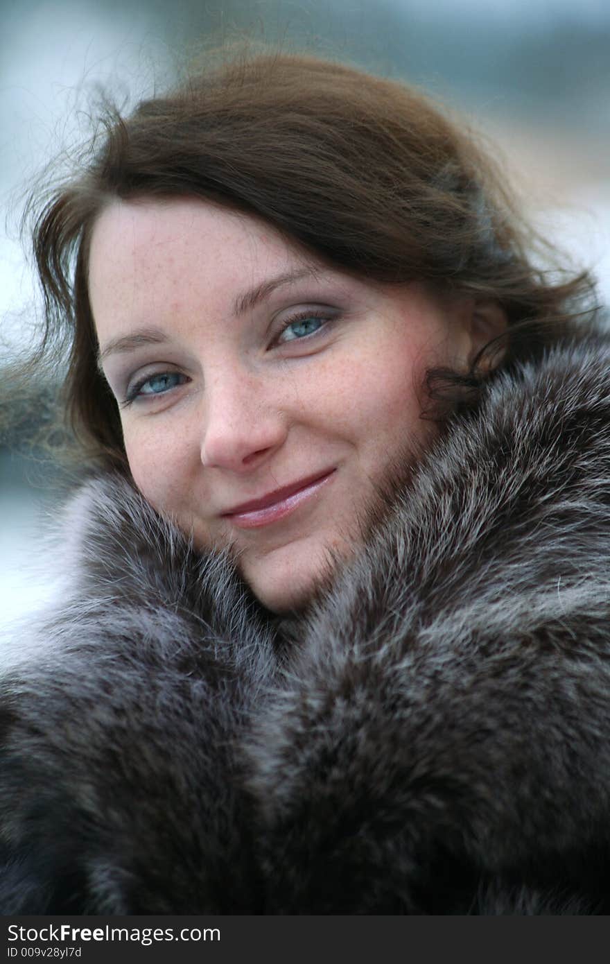 Portrait of a smiling beautiful girl in a fur coat from a raccoon on the nature