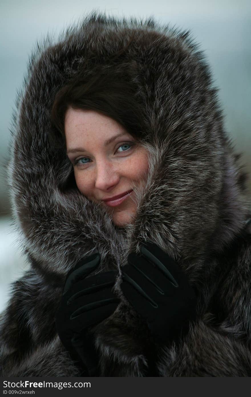 Portrait of a smiling beautiful girl in a fur coat from a raccoon on the nature