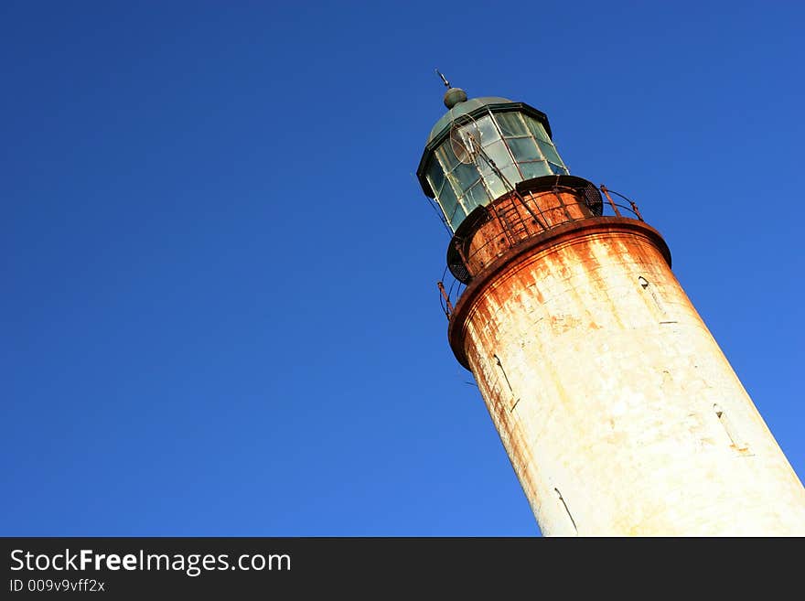 Old rusted lighthouse in front a clear blue sky.