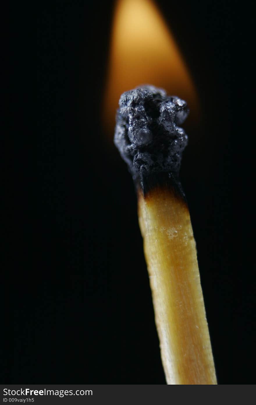 Match head on fire against black background with norrow focus on match head