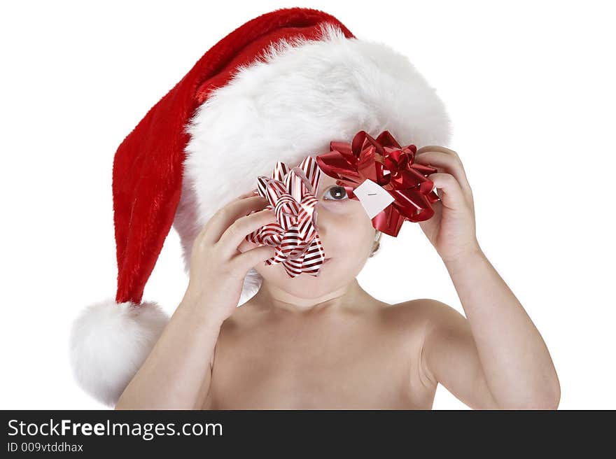 A young child wearing a santa hat and holding a red christmas bow and a red & white christmas bow. Looking at the camera though the bows, the white sticker underneath is visible. Isolated white background. A young child wearing a santa hat and holding a red christmas bow and a red & white christmas bow. Looking at the camera though the bows, the white sticker underneath is visible. Isolated white background