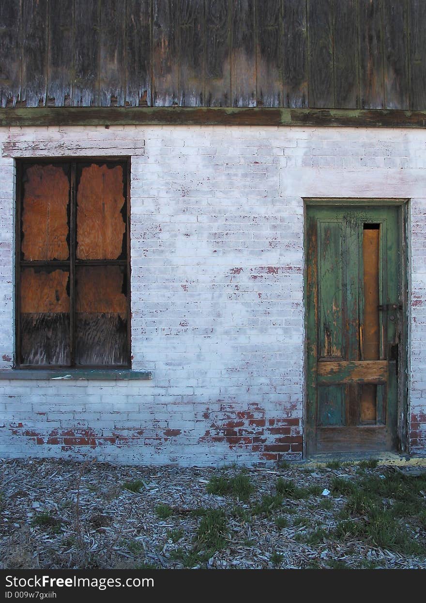 Description: Industrial image of a door and boarded-up window on a white brick background. Top-fourth of the shot is a wooden roof. Bottom-fourth of the shot is dirt/scrub-brush. Picture resembles ruins in Paris after World War II. Description: Industrial image of a door and boarded-up window on a white brick background. Top-fourth of the shot is a wooden roof. Bottom-fourth of the shot is dirt/scrub-brush. Picture resembles ruins in Paris after World War II.