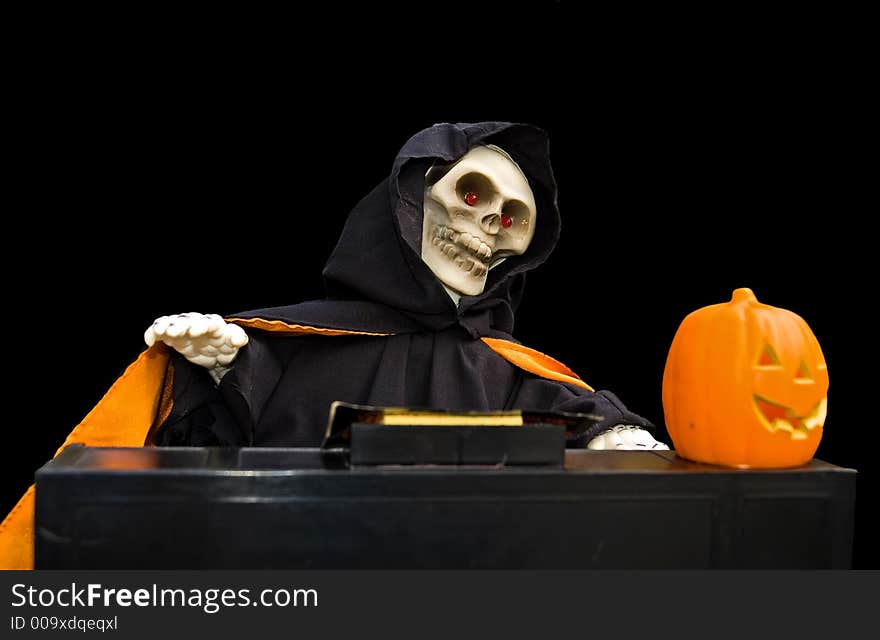 Halloween doll of a ghoul playing a piano with a carved pumpkin on it isolated on a black background. Halloween doll of a ghoul playing a piano with a carved pumpkin on it isolated on a black background