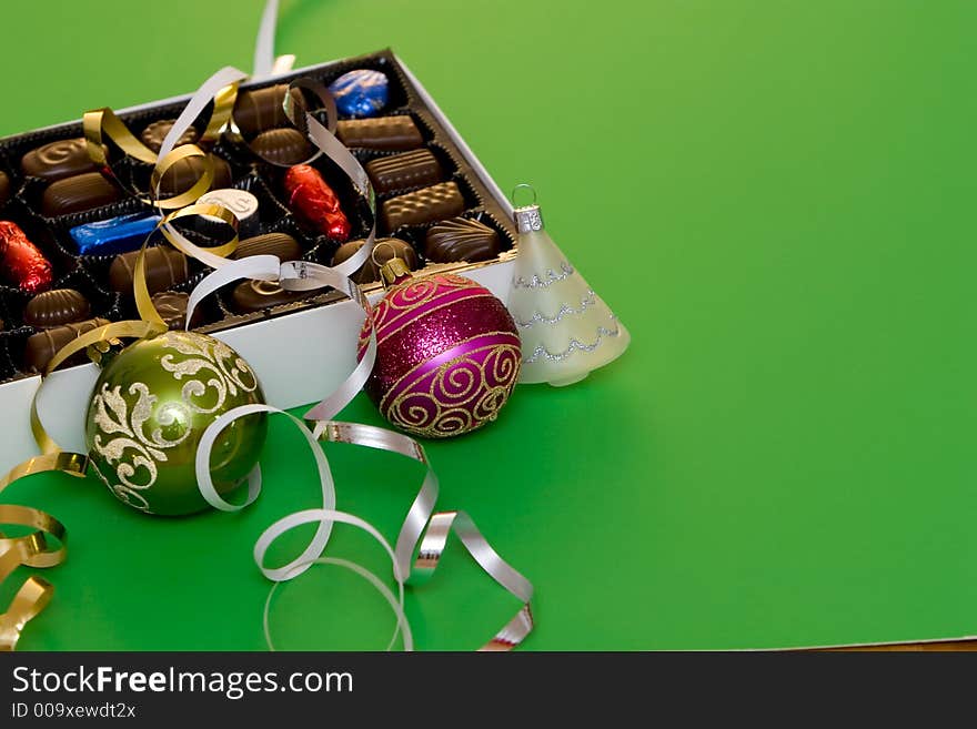 A box of fine chocolate on green background, christmas balls and decorations. A box of fine chocolate on green background, christmas balls and decorations