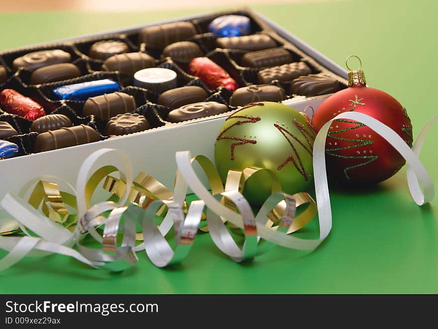 A box of fine chocolate on green background, christmas balls and decorations. A box of fine chocolate on green background, christmas balls and decorations