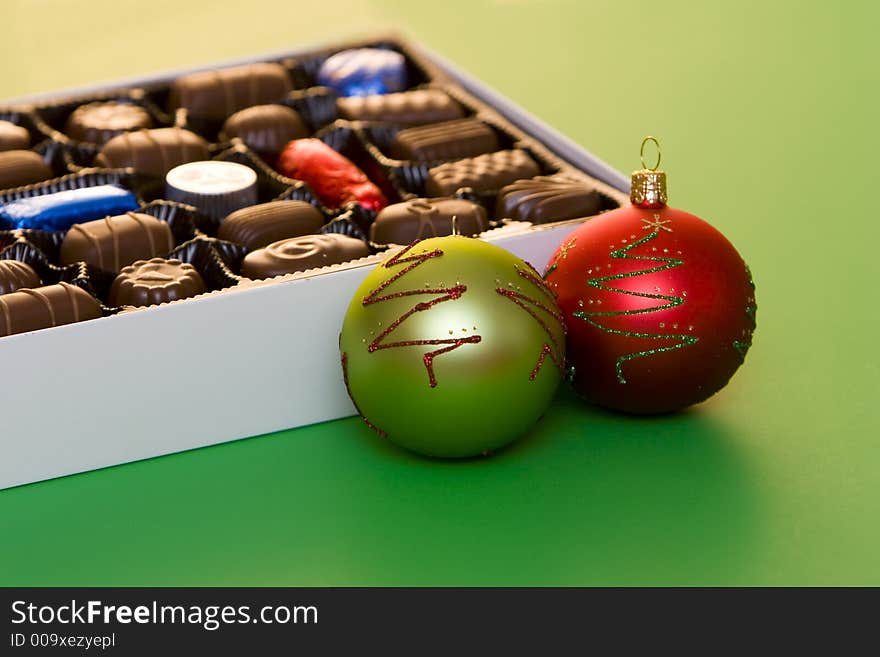 A box of fine chocolate on green background, christmas balls and decorations. A box of fine chocolate on green background, christmas balls and decorations