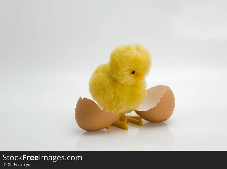 Hatched chick toy next to egg shells over white background. Hatched chick toy next to egg shells over white background