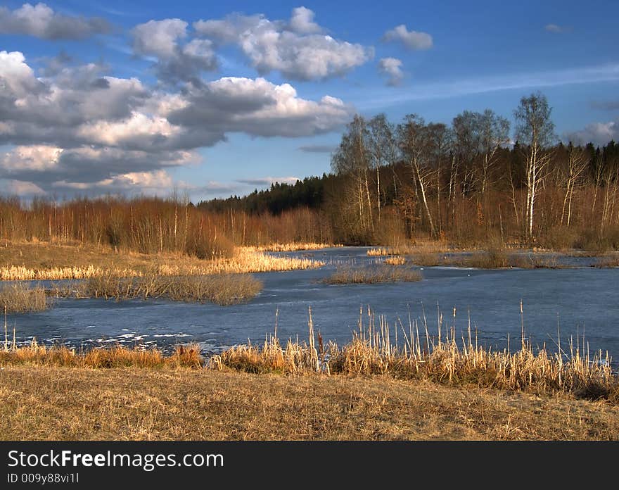 March landscape with leafless trees and frozen lake