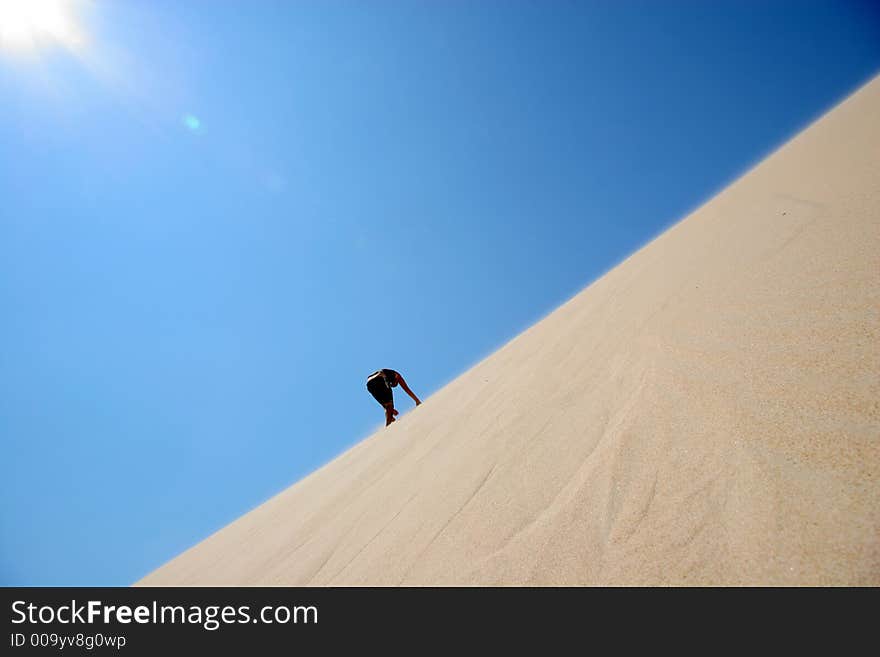 A man is climbing a sand dune in the mid day's sun. A man is climbing a sand dune in the mid day's sun