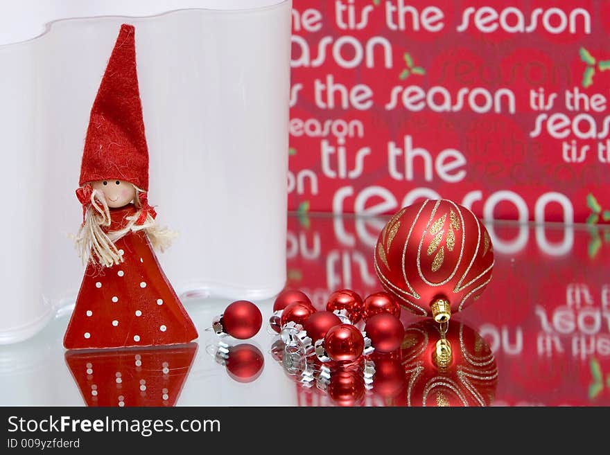 Red christmas balls on mirror red background reading tis the season and red christmas fairy standing on front of white backdrop. Red christmas balls on mirror red background reading tis the season and red christmas fairy standing on front of white backdrop