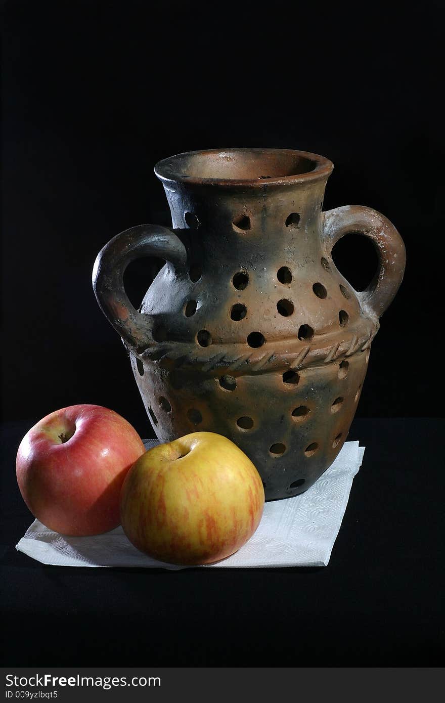 A pottery vase with a couple of apple. A pottery vase with a couple of apple