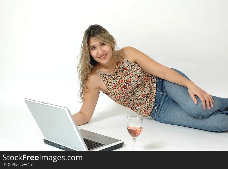 Beautiful latino woman surfing the internet chatting, emailing and reading the news on line. Woman relaxing on the floor and drinking a glass of wine as she shops on line. Woman with laptop isolated on white background.