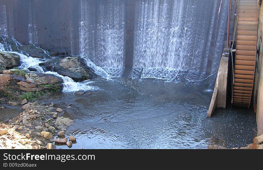 Water flowing over a dam that powers a water wheel and mill. Water flowing over a dam that powers a water wheel and mill