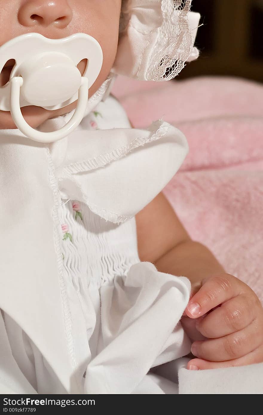 Baby girl dressed in frilly bonnet sucking on a pacifier. Baby girl dressed in frilly bonnet sucking on a pacifier.