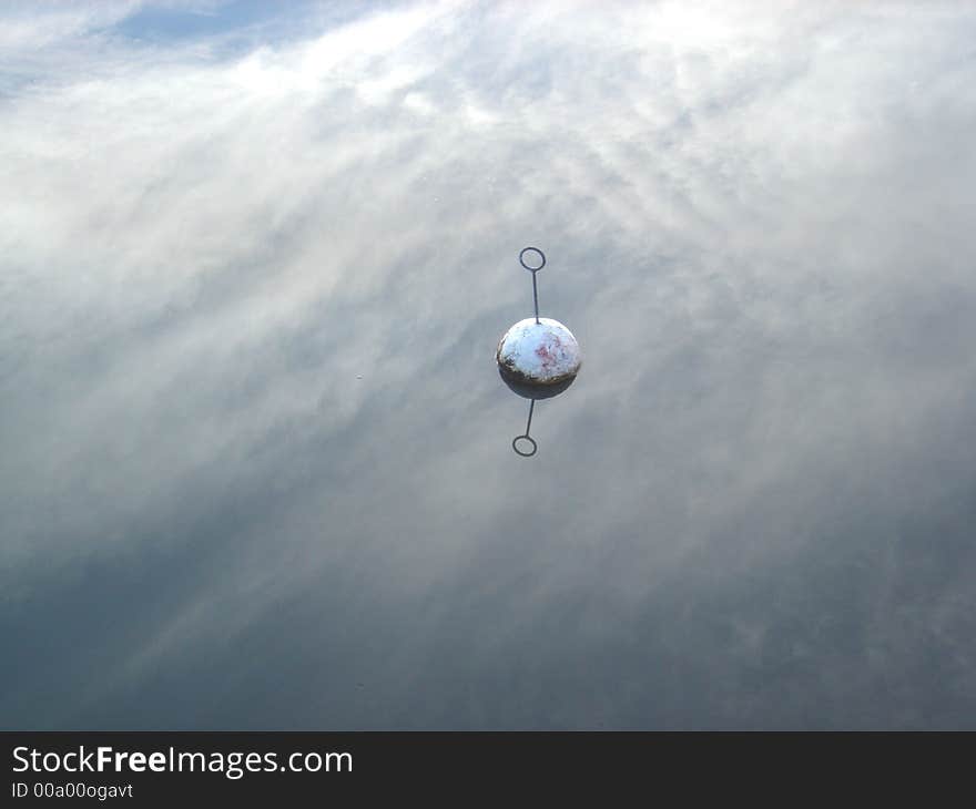 An old floating buoy in totally still water reflecting the sky covered with feathery clouds. An old floating buoy in totally still water reflecting the sky covered with feathery clouds