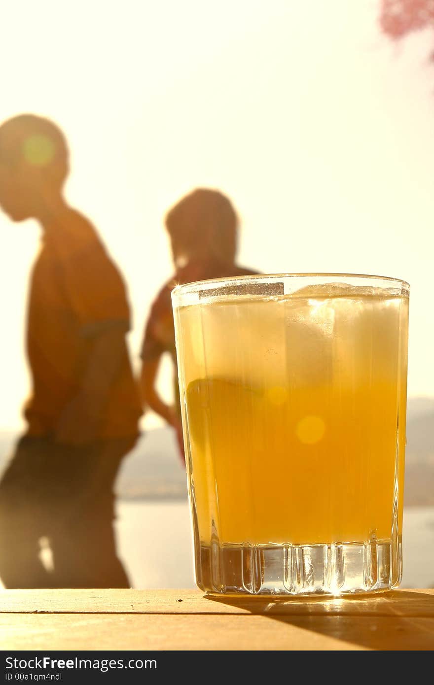 Ka glass of orange juice with children holding hands in the background. Ka glass of orange juice with children holding hands in the background