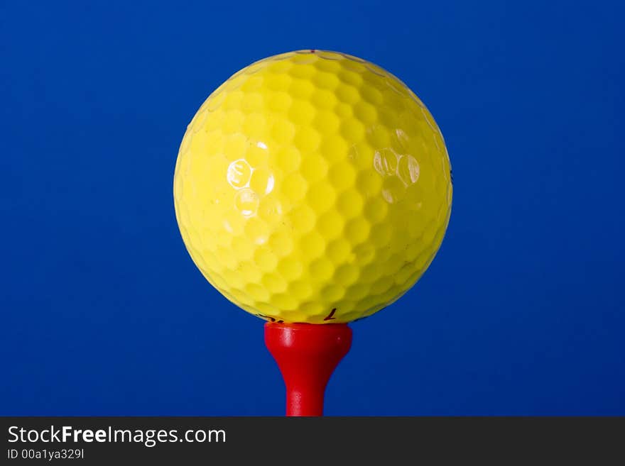 Yellow Golf ball on red tee against blue background photographed in studio