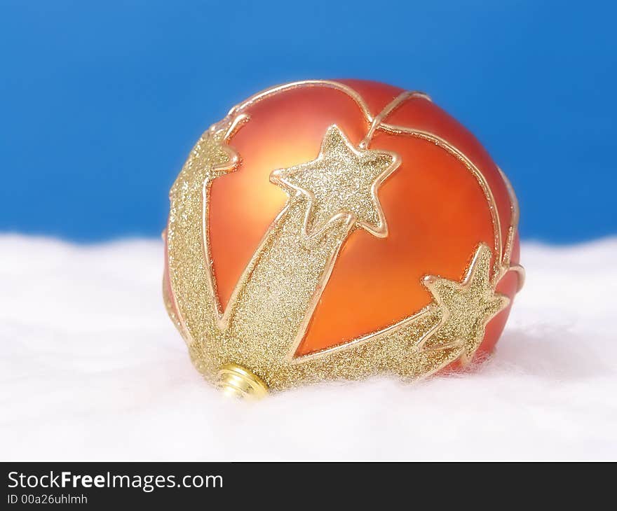 Orange christmas ball arranged with golden ornaments on white fluffy surface over blue background