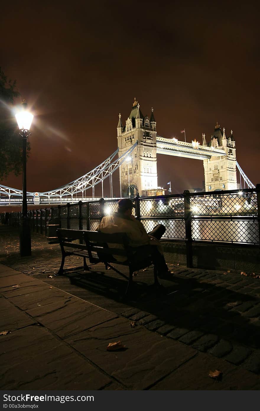 Man sitting on a bench in front of The Tower Bridge at night in London, UK. Man sitting on a bench in front of The Tower Bridge at night in London, UK