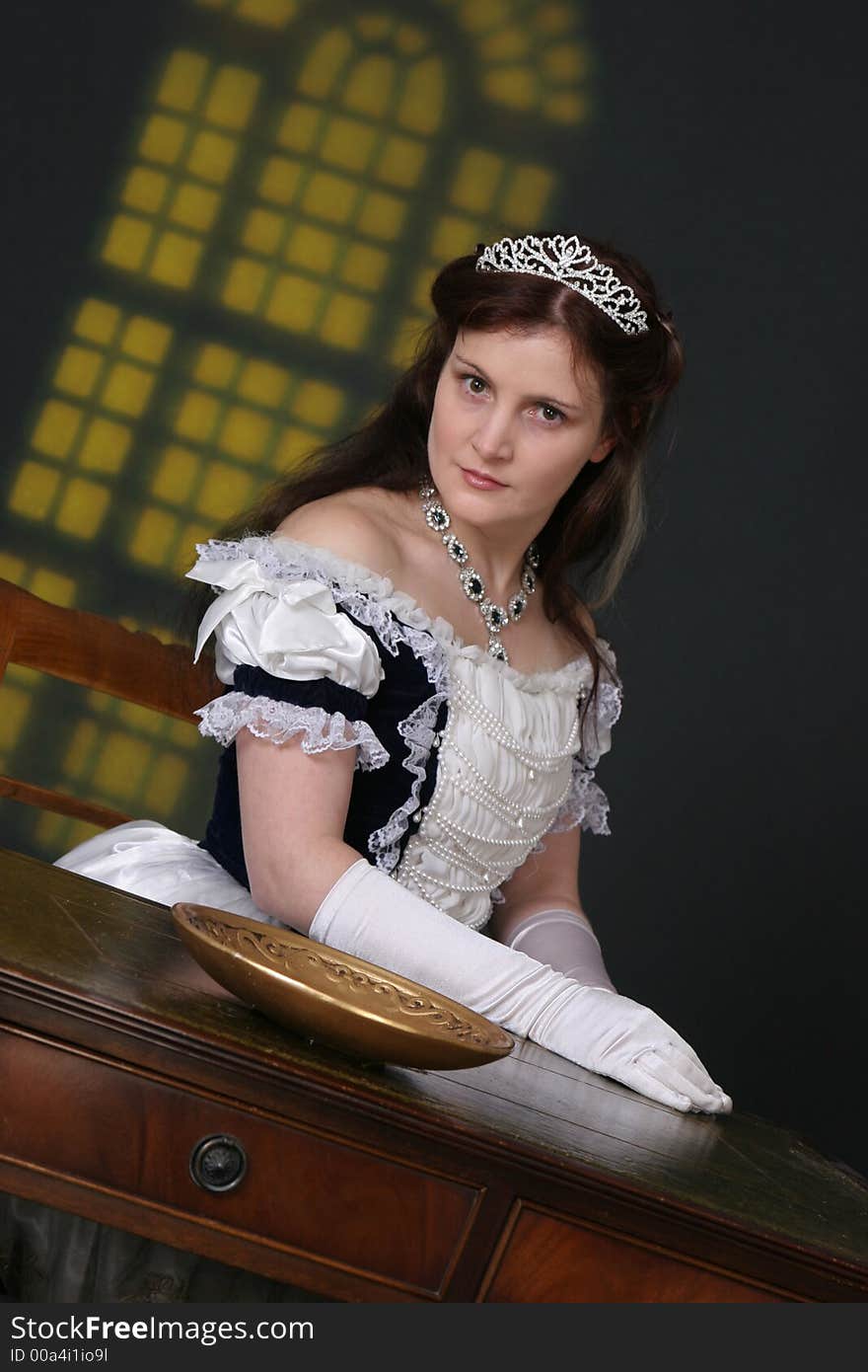 Girl in historic robe sitting at table in front of yellow window