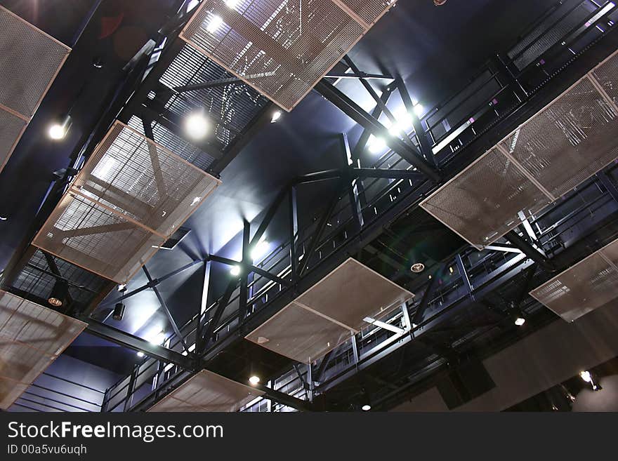 Steel structure of the ceiling of a theater. Spotlights and fluorescent lamps create an extravagant atmosphere onto the staff footbridges. These are used to place focus or moving parts involved in the plays by attaching them to the steel beams. Steel structure of the ceiling of a theater. Spotlights and fluorescent lamps create an extravagant atmosphere onto the staff footbridges. These are used to place focus or moving parts involved in the plays by attaching them to the steel beams.