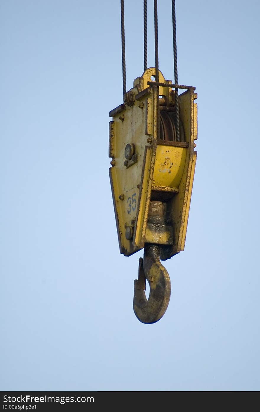 A yellow crane hook hanging from cables. A yellow crane hook hanging from cables