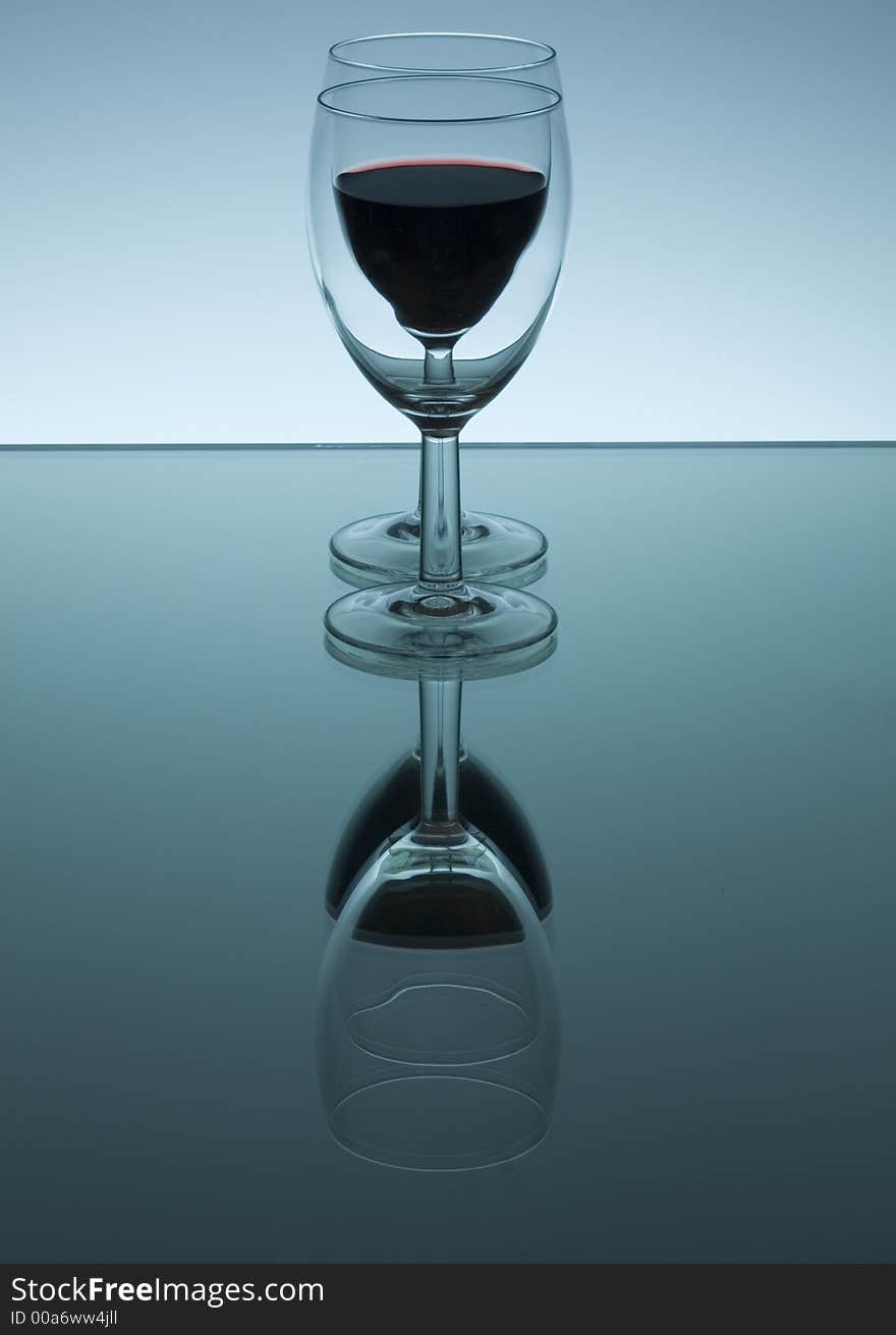 A glass filled with red wine reflected in a mirror. A glass filled with red wine reflected in a mirror.